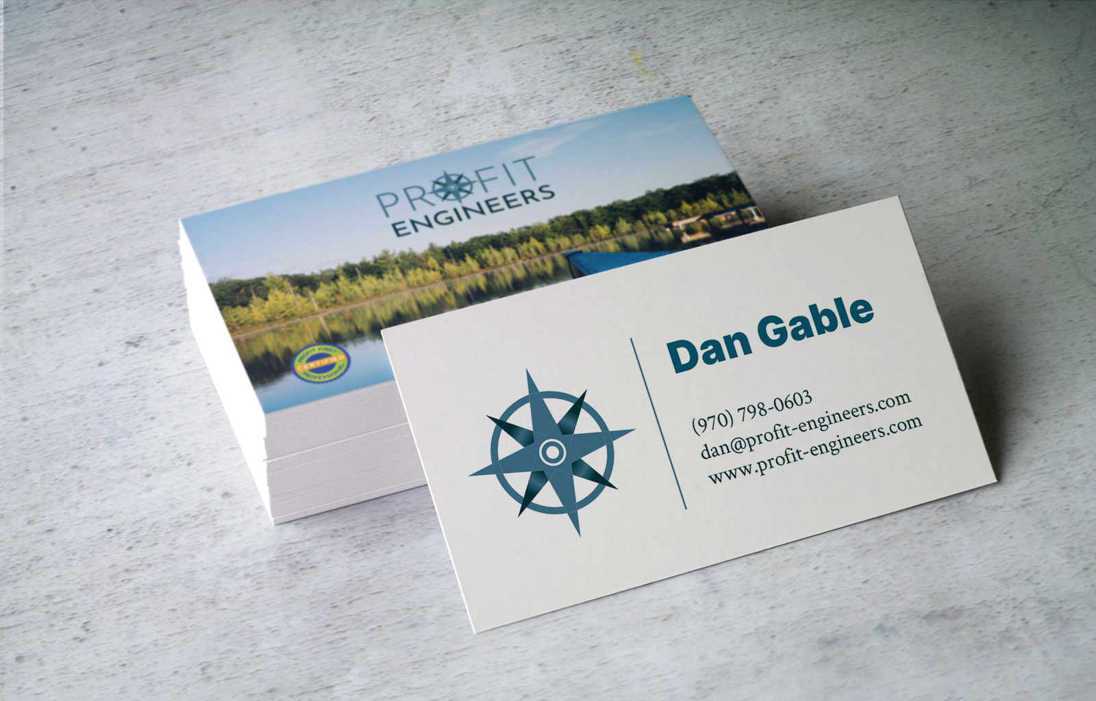 Double sided business card for profit Engineering One side has company logo and photo of a canone on the lake, other side compass icon and company info