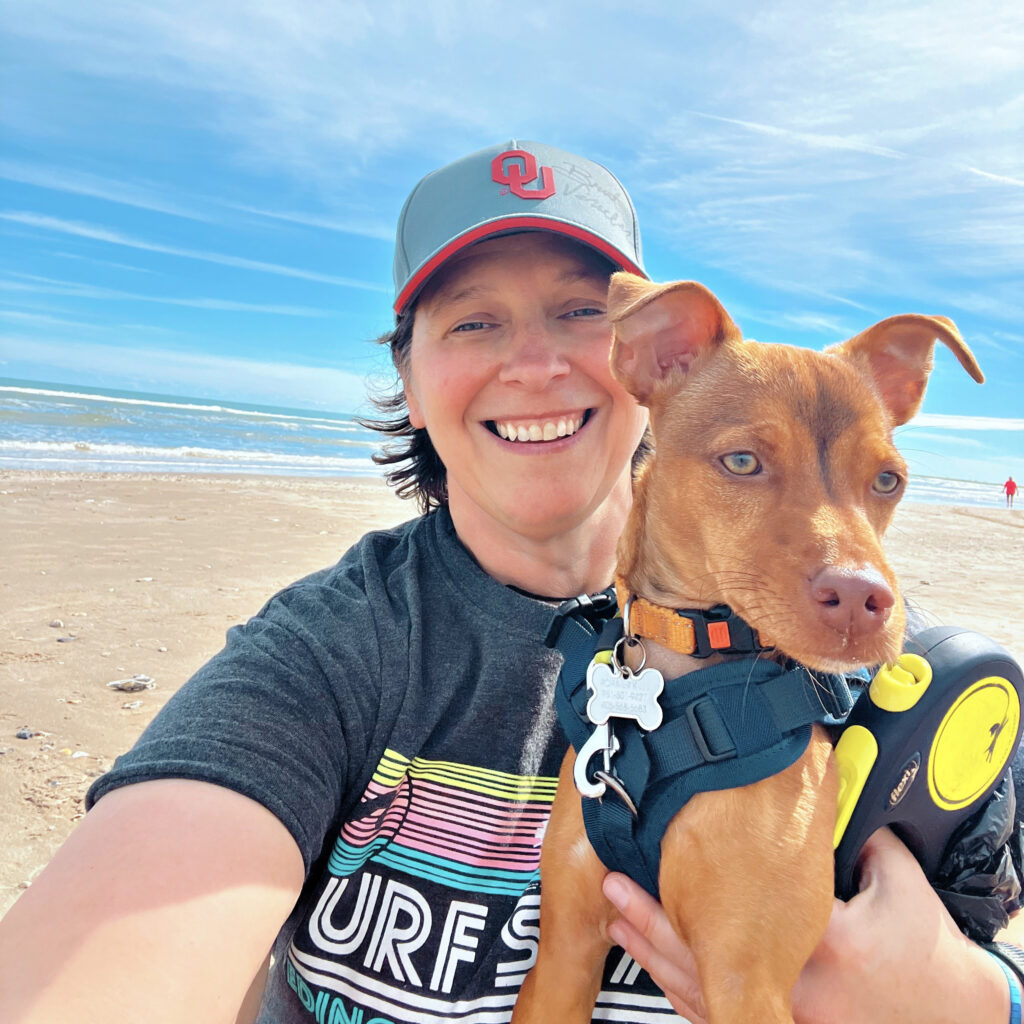 Self of Mandy Love graphic design on the beach in South Padre Island, holder her small 15 pound chihuahua mix Roamer